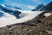 The way to the Aktru glacier. Snowy high-altitude plateau. Alpine landscape with snow-capped mountain peak and sharp rocks under blue sky. Colorful sunny mountain scenery with snow mountain top.