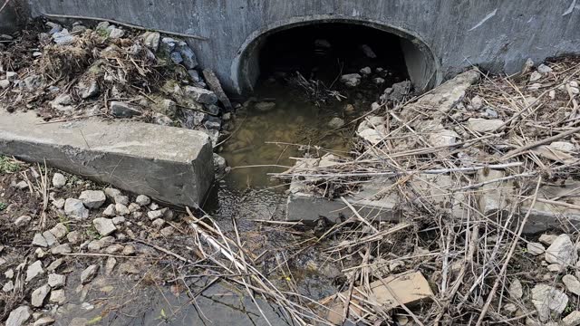 Concrete drainage ditch and pipe with flowing clear water