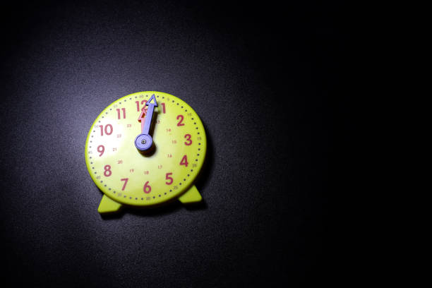 yellow toy clock on dark background showing 12 o'clock. top and closeup view.