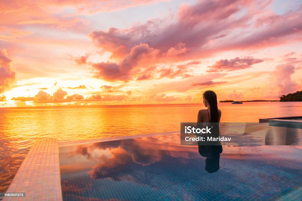 Paradise sunset idyllic vacation woman silhouette swimming in infinity pool looking at sky reflections over ocean dream. Perfect amazing travel destination in Bora Bora, Tahiti, French Polynesia. Swimming Pool Stock Photo