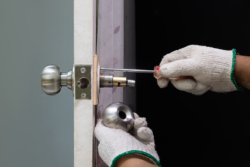 Locksmith on wood door with screwdriver for repair or fix silver knob.