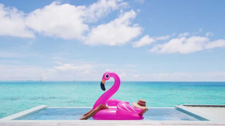 Travel vacation holidays concept. Woman in pool by beach sunbathing in bikini in inflatable pink flamingo toy mattress float in. Girl relaxing enjoying luxury lifestyle at resort pool.