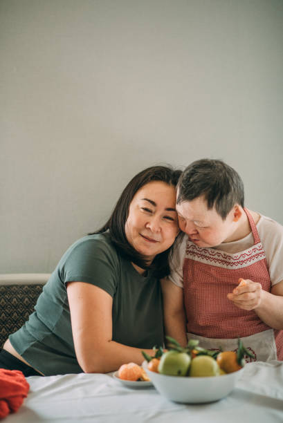 An elderly woman with down syndrome gently leans against an Asian woman of 40 years. The concept of support and relationships stock photo