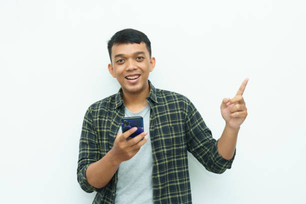 istock Young Asian man smiling and holding smartphone while other hand pointing to left side 1482514539
