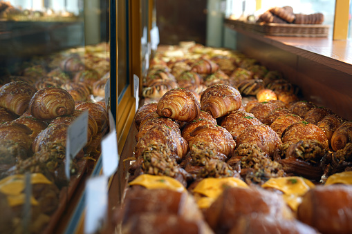 View of various baked pastry and bread bun in glass cabinet at bakery shop. Fresh snacks displayed for sale in a coffee shop.