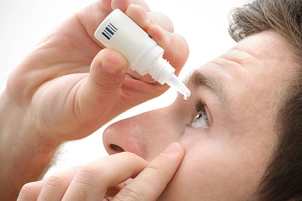 Dripping eye with eyes drops Closeup view of young man applying eye drop eyedropper stock pictures, royalty-free photos & images