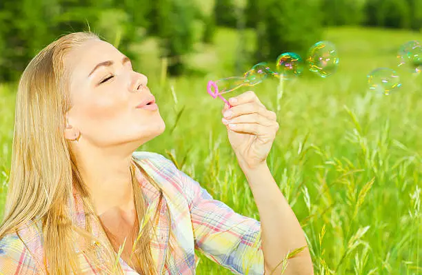 Pretty woman blowing soap bubbles in park, healthy beautiful female playing on green grass, carefree model relaxing outdoors, cute teen enjoying leisure time, vacation and summer holiday concept