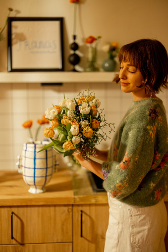 Beautiful woman makes a bouquet of flowers on kitchen at home, decorating her modern apartment with fresh flowers