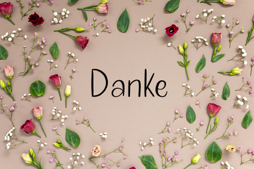 Flower Arrangement With German Text Danke Means Thank You. Colorful Spring Blossoms And Flowers Like Roses Building A Frame. Flat Lay With Brown Paper Background