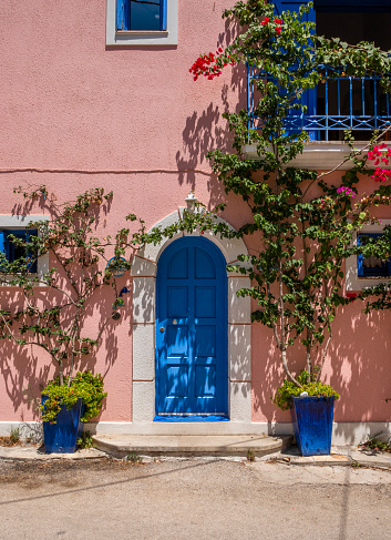 Wooden door closed and three glass windows with open shutters blue color on white wall background. Cyclades island house front view, Greek traditional architecture.