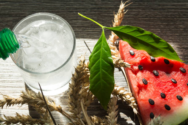 A triangular piece of sweet watermelon on an ice cream shelf, a cold drink with ice and ripe wheat ears on a wooden surface.,,