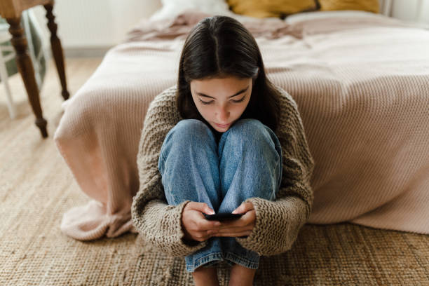 Teenage girl sitting on the floor and scrolling her smartphone. stock photo