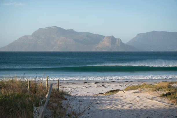 Long Beach, Kommetjie A small wave feathers and breaks at Long Beach, in Kommetjie, Cape Town, with the mountains of Table Mountain National Park in the background. kommetjie stock pictures, royalty-free photos & images