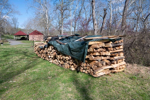 Rural rustic scene of a row of chopped and  stacked cord of wood cordwood with a big barn and country nature background. No people, with copy space.