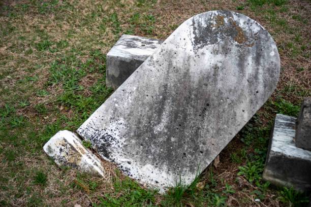 istock Toppled ancient gray gravestone partially buried surrounded by grass 1482556901