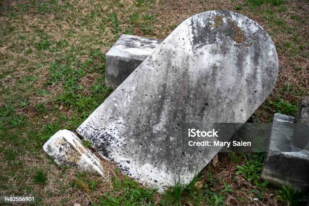 Toppled Ancient Gray Gravestone Partially Buried Surrounded By Grass Stock Photo - Download Image Now