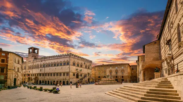 An idyllic sky at sunset of Piazza IV Novembre, the main square in the medieval neighborhood of Perugia, capital of Umbria, central Italy. In the center, the majestic Palazzo dei Priori, considered one of the greatest examples of public palace architecture in Italy. Still today the seat of the Municipality of Perugia (Town Hall), the building was built between 1293 and 1443 and inside it preserves works and frescoes by great artists, such as Pinturicchio, the Perugino, Raffaello and Benedetto Bonfigli. Always in the center, the Fontana Maggiore (Mayor Fountain), built in 1275 as a terminal of the medieval aqueduct, is composed of two polygonal marble basins concentric decorated with bas-reliefs sculpted by Nicola and Giovanni Pisano. On the right, the stairway and the side stone façade of the Duomo di San Lorenzo (Cathedral of Saint Lawrence), built in Gothic style starting from 1345 and completed in 1490 and characterized by its splendid pink marbles. Founded by the Etruscans on an ancient Umbrian settlement, Perugia is one of the most loved and visited medieval Italian cities, rich in artistic and architectural treasures that span almost three thousand years of history. The Umbria region, considered the green lung of Italy for its wooded mountains, is characterized by a perfect integration between nature and the presence of man, in a context of environmental sustainability and healthy life. In addition to its immense artistic and historical heritage, Umbria is famous for its food and wine production and for the high quality of the olive oil produced in these lands. Super wide angle image in 16:9 ratio and high definition quality.
