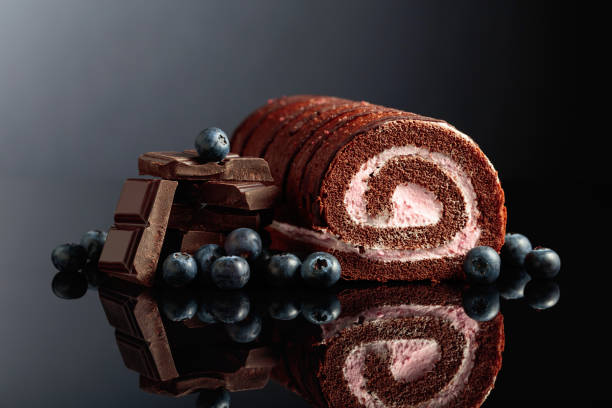 Chocolate roll cake with blueberries and a broken black chocolate bar.