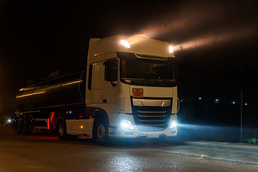 Tanker truck with dangerous goods on a foggy night with high beam lights on. Close-up.