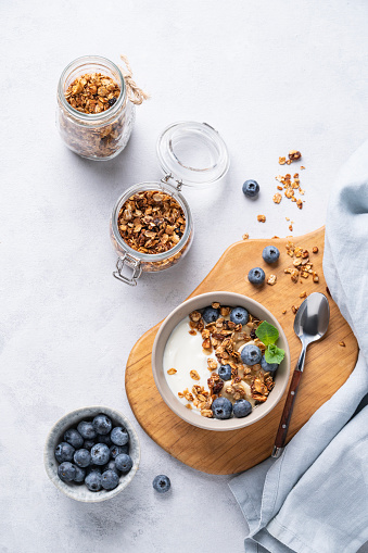 The concept of a healthy breakfast of yogurt, granola and fresh blueberry on a light background. Homemade diet and protein food. Top view and copy space.