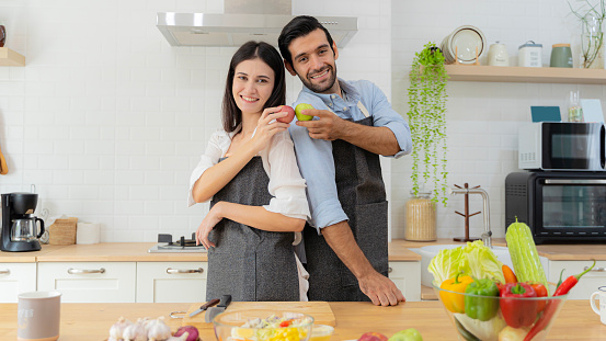 Attractive couple holding red apples and green apples in their hands. A young couple in love having fun while preparing a breakfast together on a beautiful morning. Cooking, together, kitchen.