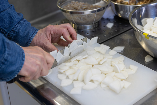 Close up of a mans hands chopping up daikon to make miso soup on a cutting board in a kitchen.