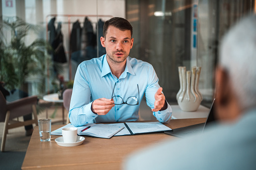 Caucasian HR manager interviewing a mature Hispanic male job applicant. Sitting at a desk in a modern office.