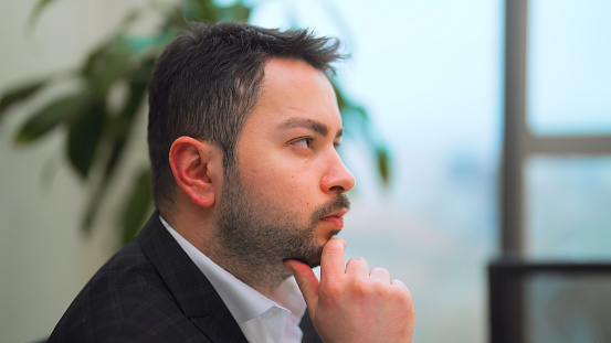 A young businessman is thinking over his business and making plans in his office.