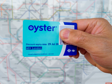 London. UK- 09.14.2021: A hand holding a 60 plus photo oyster card with the map of London underground and overground map in the background.