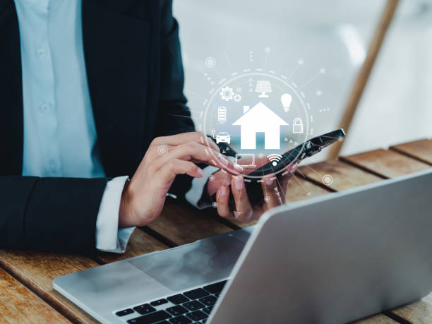 istock Smart home technology concept. Virtual screen of futuristic smart home digital management icons and symbols on smart mobile phone holding by businessman's hand while working with laptop in office. 1482582663