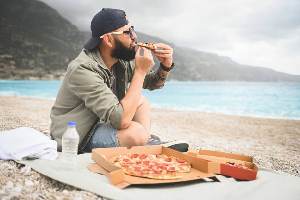 istock man resting on the beach and eat pizza 1482583828