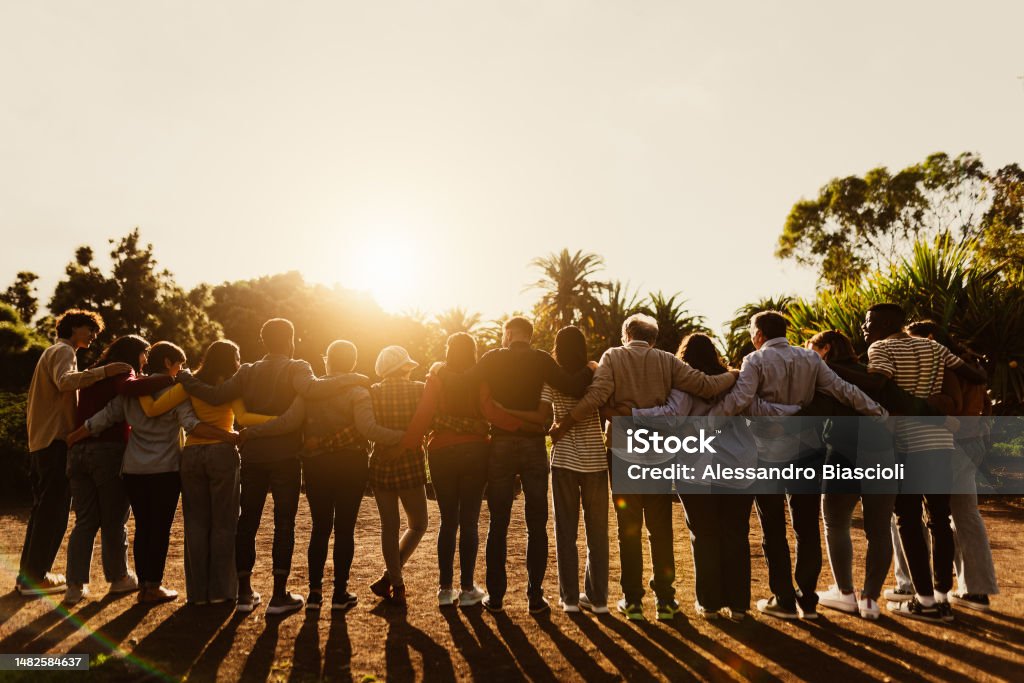 Back view of happy multigenerational people having fun in a public park during sunset time - Community and support concept Community Stock Photo