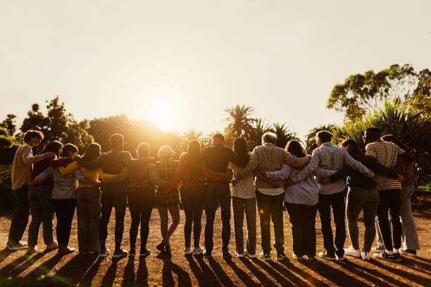 Back view of happy multigenerational people having fun in a public park during sunset time - Community and support concept stock photo