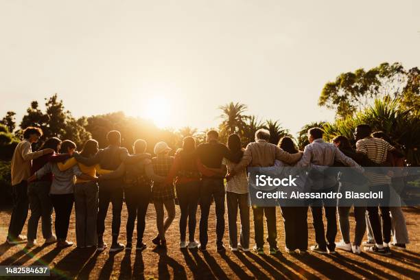 Back View Of Happy Multigenerational People Having Fun In A Public Park During Sunset Time Community And Support Concept Stock Photo - Download Image Now