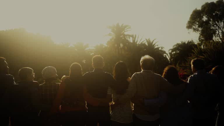 Back view of happy multigenerational people having fun in a public park during sunset time - Community and support concept