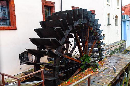 A wooden water wheel or watermill turbine milling, grinding, turning, and generating power, perhaps as a traditional alternative energy source. Positioned against the stone wall of a cottage building exterior, located in St. Paul, Minnesota, USA.