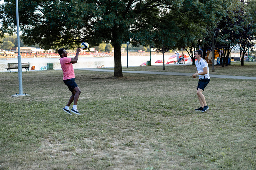 Two male soccer players in professional sports attire compete in an outdoor stadium. One performs a high kick whilst the other attempts a tackle on the field. The night setting suggests a competitive match atmosphere.