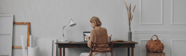 istock Rear view of young woman using smart phone while working at her home office 1482587830