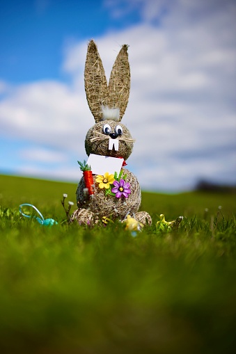A vertical shot of a thatched rabbit toy with flowers in a field for Easter
