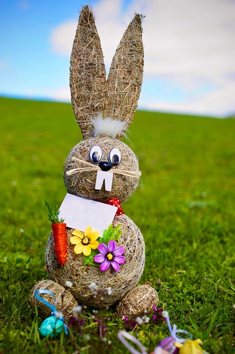 A vertical shot of a thatched rabbit toy with flowers in a field for Easter