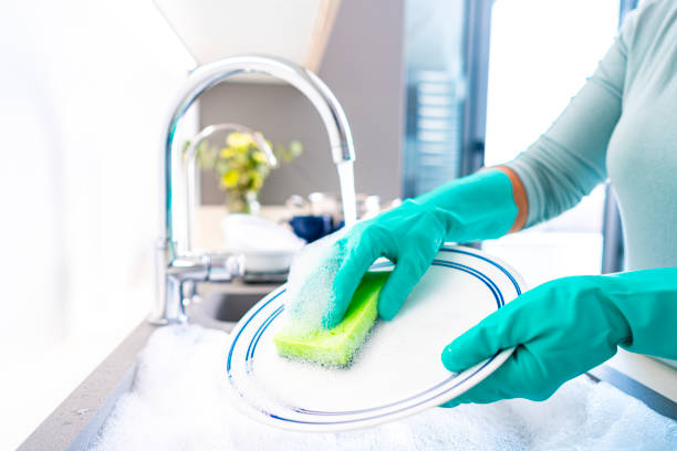 Close up of woman's hands wearing washing up gloves washing a dish with a sponge under flowing water in a kitchen sink. High resolution 42Mp indoors digital capture taken with SONY A7rII and Zeiss Batis 25mm F2.0 lens