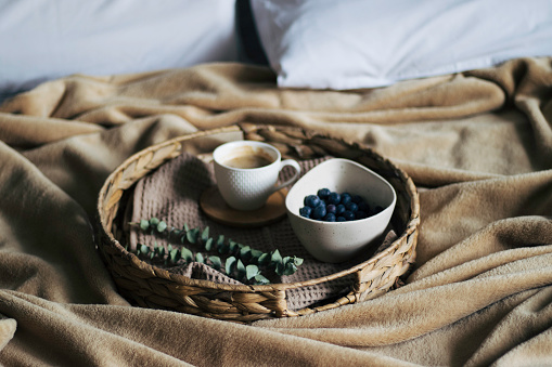 Breakfast in bed concept. Coffee with milk in a white cup and fresh blueberry on a wooden  tray. Eating in bedroom. Morning coffee