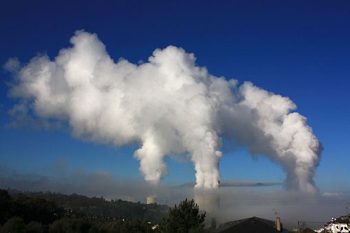 Chimneys and thick white smoke with blue sky background. As Pontes, A Coruña province, Galicia, Spain.