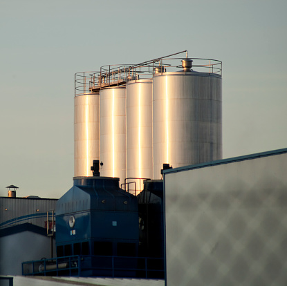 Stainless Steel storage tanks in a dairy factory at dusk, built structures  in the foreground, sky background.