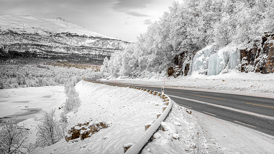 Winter coastal road of Tromso,Norway while snow covered tree and waterfall was frozen.