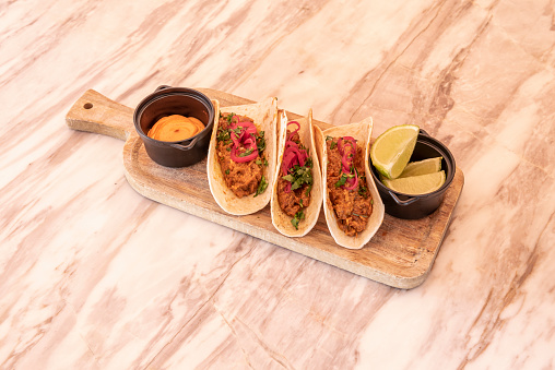 Typical Mexican recipe of cochinita pibil tacos with lime, red onion and salsa on a pink marble table