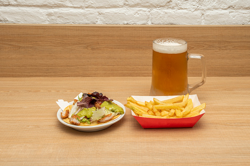 Mariachi taco menu with fried chicken battered with guacamole and lettuce, portion of chips and a mug of cold beer on wooden table