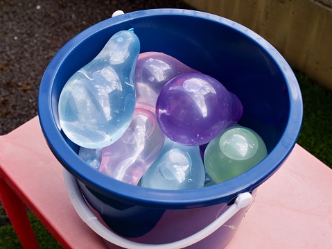 Blue bucked filled with colorful water balloons on red table.