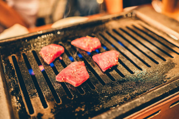 A hot iron grill with four pieces of wagyu beef being grilled on it. The Japanese-style grilled beef is a popular dish in which high-quality beef is grilled to perfection on an iron grill, and then served with various dipping sauces and side dishes.