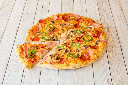 Small Thin Crust Pizza with Mushrooms, Ham, Sliced Green Peppers and Spicy Pepperoni with Mozzarella Cheese and a Cut Slice